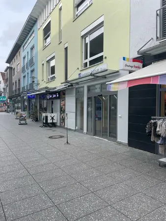 Moderne Einkaufsstraße mit bunten Gebäuden, Modegeschäft und Glasfaserzentrum bei Tageslicht.