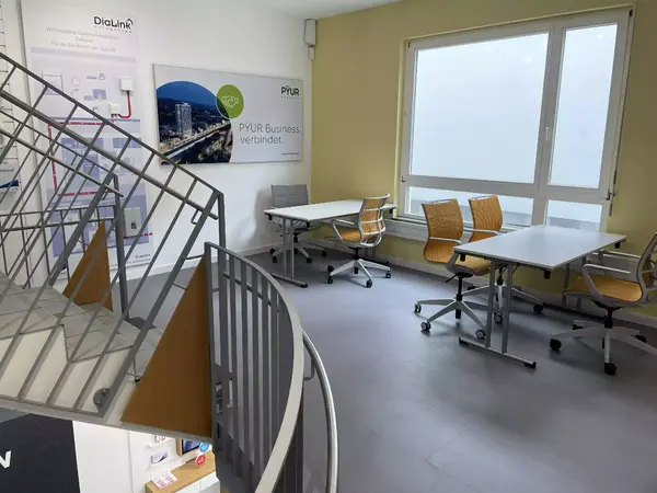 Moderner Besprechungsraum mit Konferenztischen, Bürostühlen und großem Fenster.